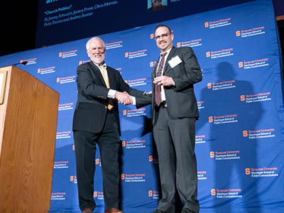 Two men standing on stage shaking hands. 